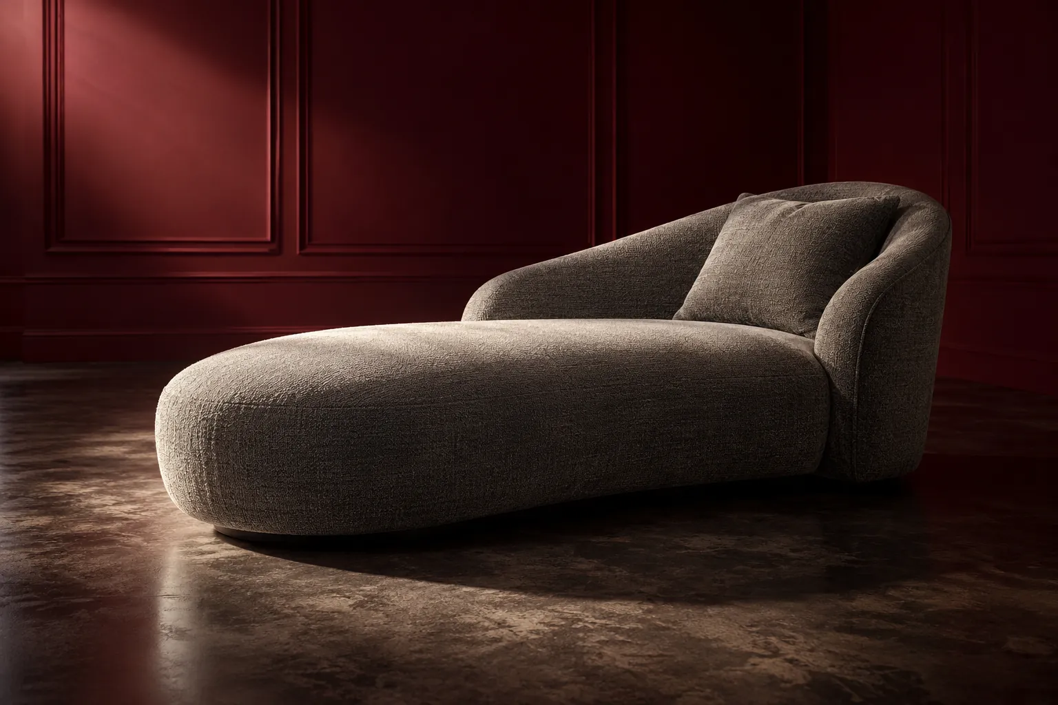 Asymmetrical grey chaise in a burgundy studio with focused lighting